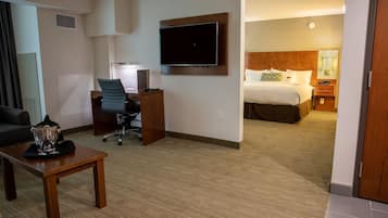 A hotel room with a bed, a desk with a chair, a TV mounted on the wall, and a small table with a pitcher.