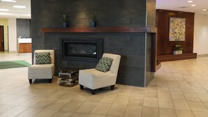 Een moderne lobby met een open haard, twee fauteuils, een bijzettafeltje en een receptiebalie.