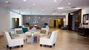 Een moderne lobby met witte fauteuils, een receptiebalie en een decoratieve wand.