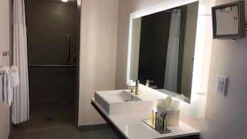 Un baño moderno con cabina de ducha a ras de suelo, un espejo grande y un mueble lavamanos con lavabo y artículos de aseo.