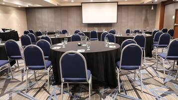 A conference room with round tables, blue chairs, and a large screen.