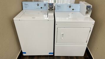 Two Whirlpool front-loading washing machines in a corner with a wooden floor and beige walls.