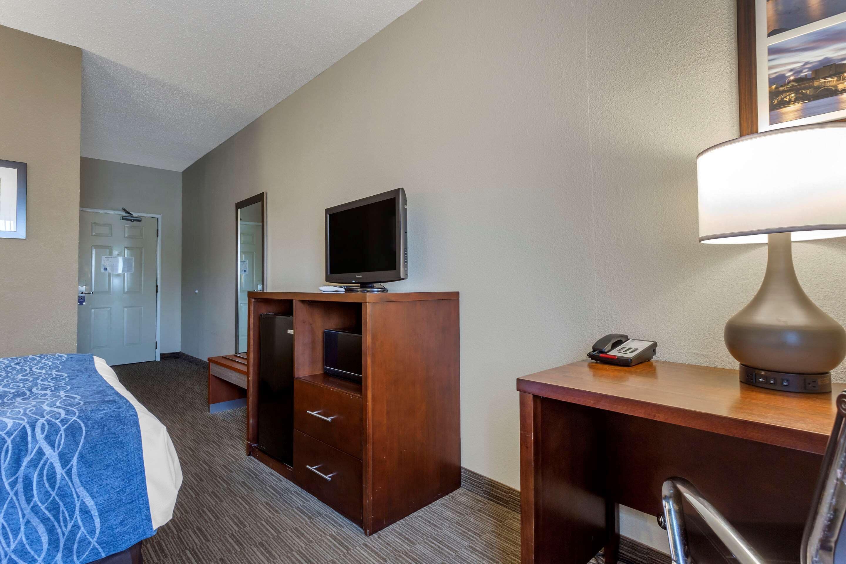 A hotel room with a bed, a desk with a lamp, a television, and a phone.