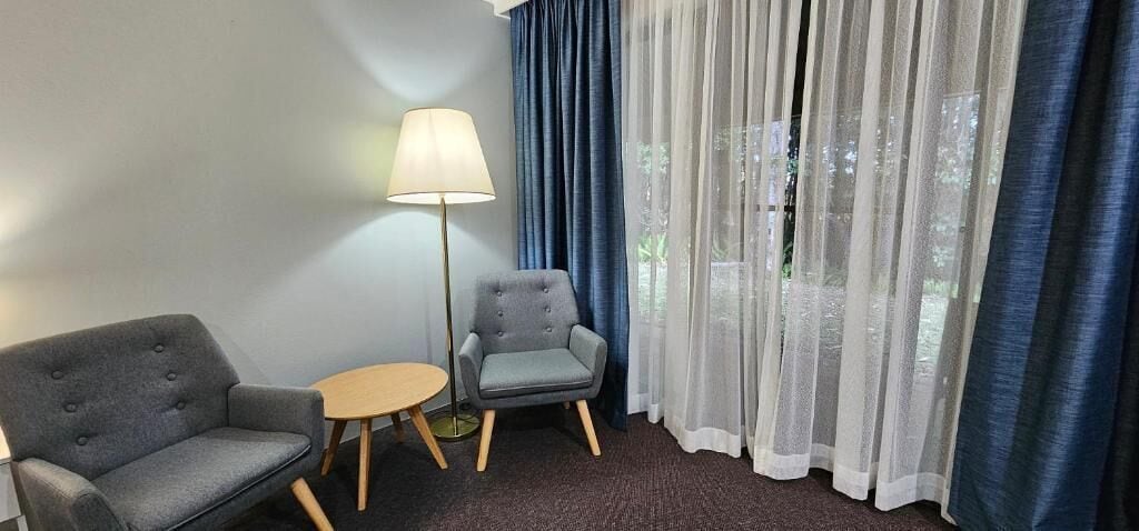 Une pièce comprenant deux fauteuils gris, une petite table ronde et un lampadaire.