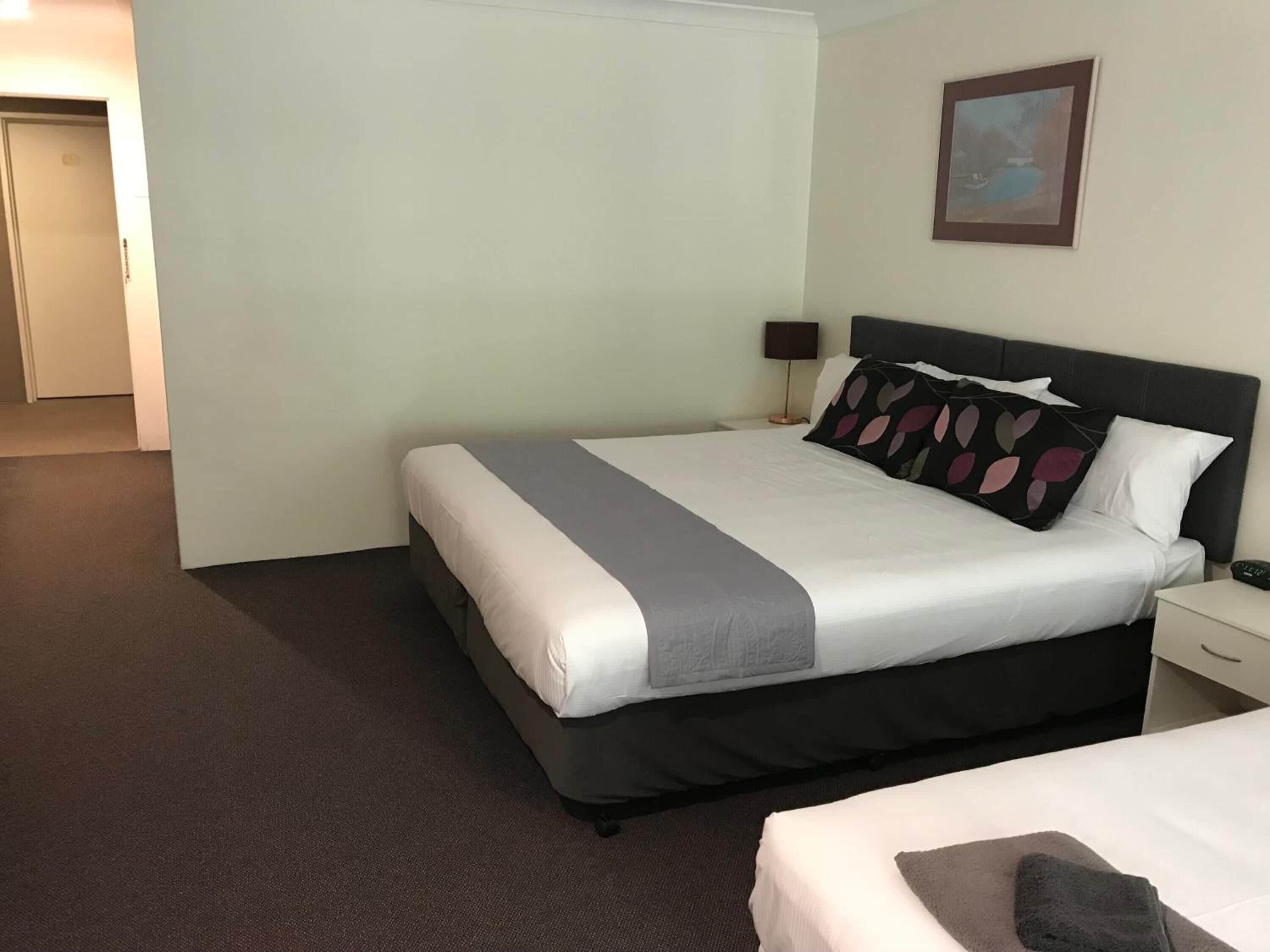 A hotel room with a large bed, a nightstand, a lamp, and a painting on the wall.