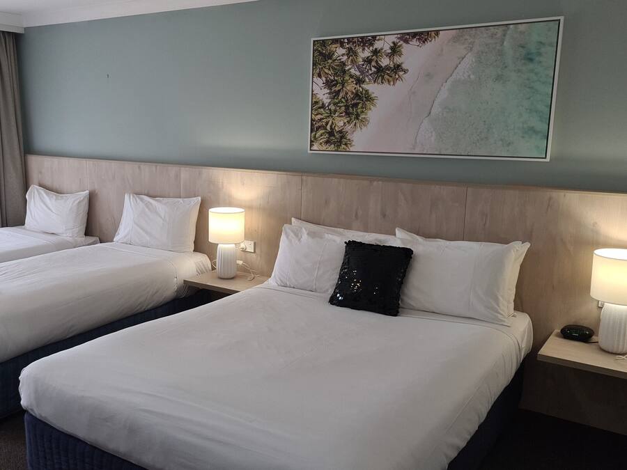 A hotel room with two beds, a wooden headboard, a painting of a beach, and a window with curtains.