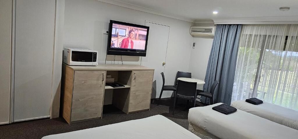 A hotel room with a bed, a desk with a TV, a chair, and a window with curtains.
