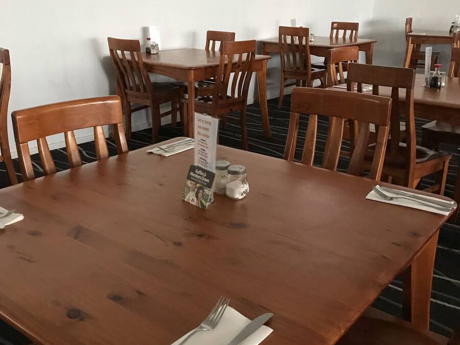 A dining area with wooden tables and chairs, a menu stand, and a television screen on the wall.