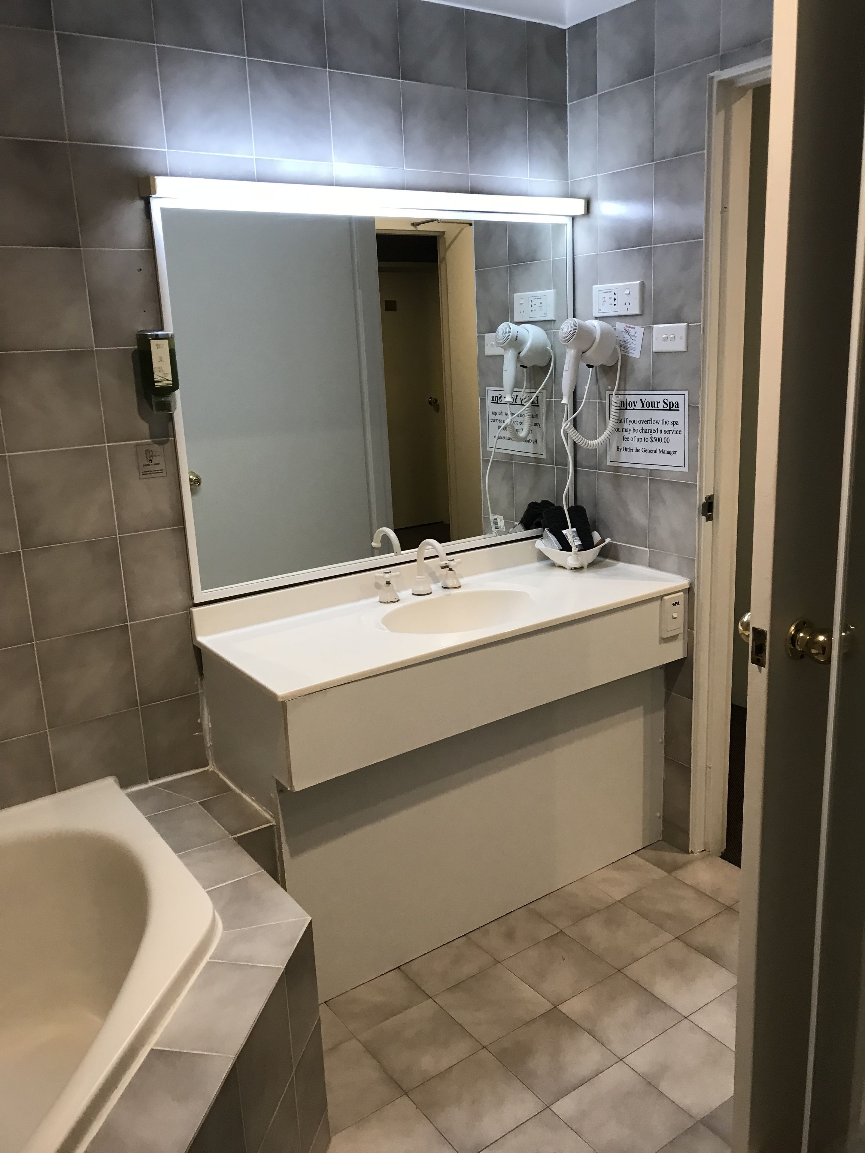 A modern bathroom with a large mirror, a white sink, and a hairdryer.