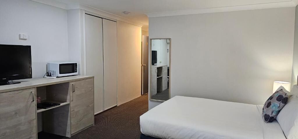 A hotel room with a bed, a TV, a microwave, a wardrobe, and a small kitchenette.