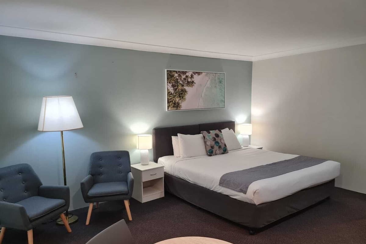 A hotel room with a large bed, two bedside tables, a chair, a round table, and a lamp.