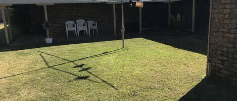 A covered outdoor area with a lawn, a metal roof, and a brick building.