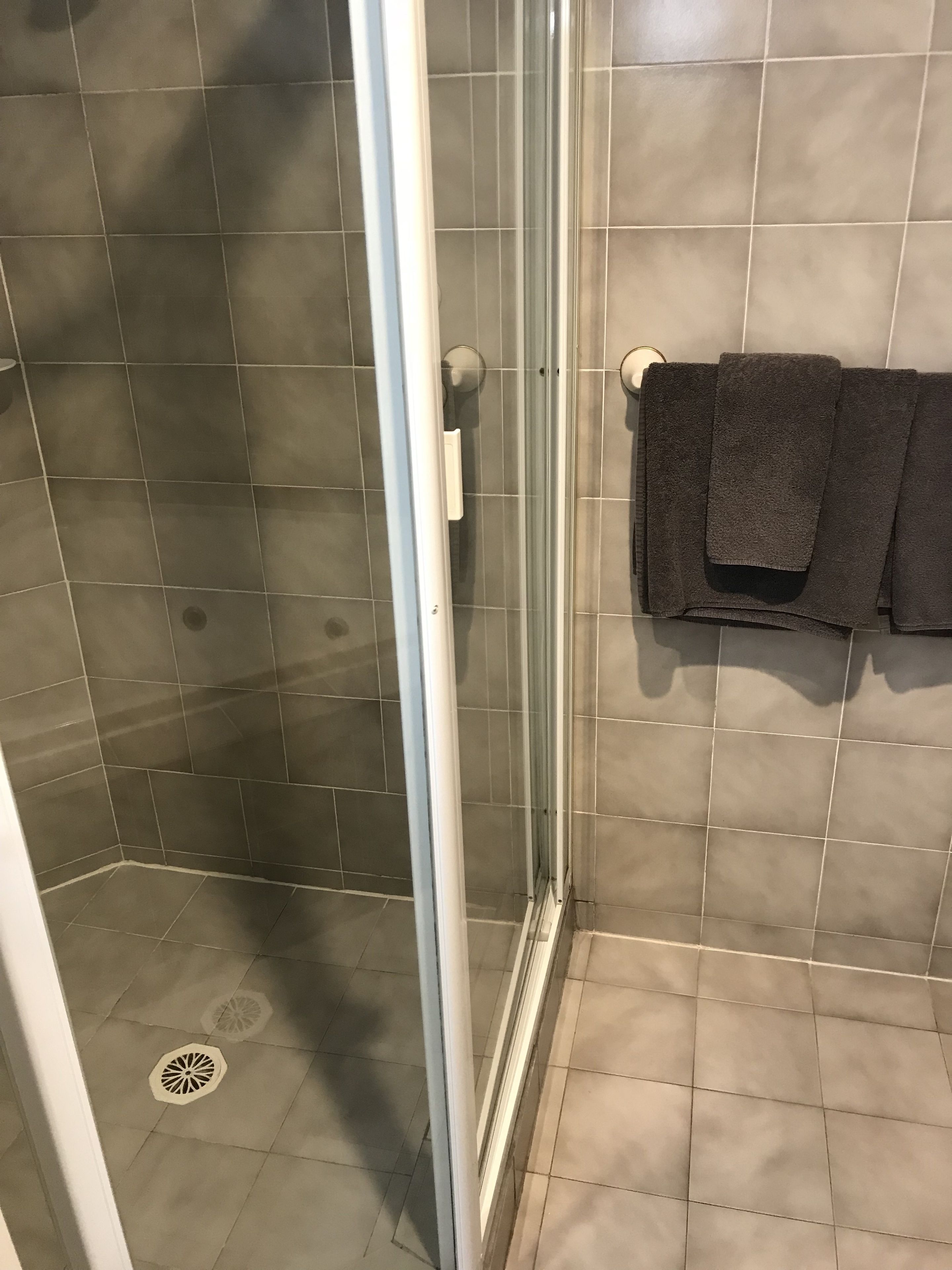 Un área de ducha con puerta de vidrio, paredes con azulejos y un perchero con toallas dobladas.