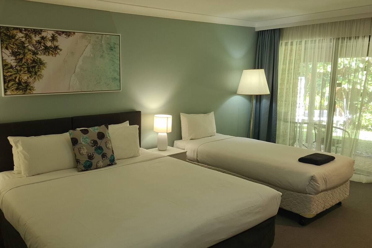 A hotel room with two beds, a nightstand with a lamp, a painting on the wall, and a window with curtains.