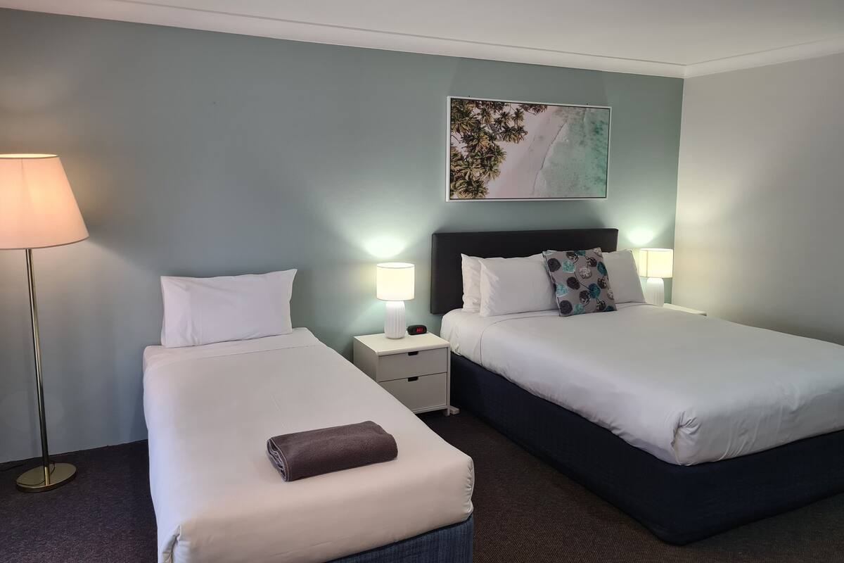 A hotel room with two beds, a nightstand, a lamp, and a painting on the wall.