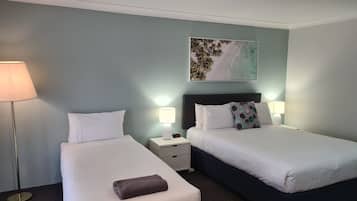 A hotel room with two beds, a nightstand, a lamp, and a painting on the wall.
