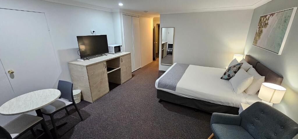 Ett hotellrum med en säng, ett skrivbord, en stol, en tv och ett litet bord.
