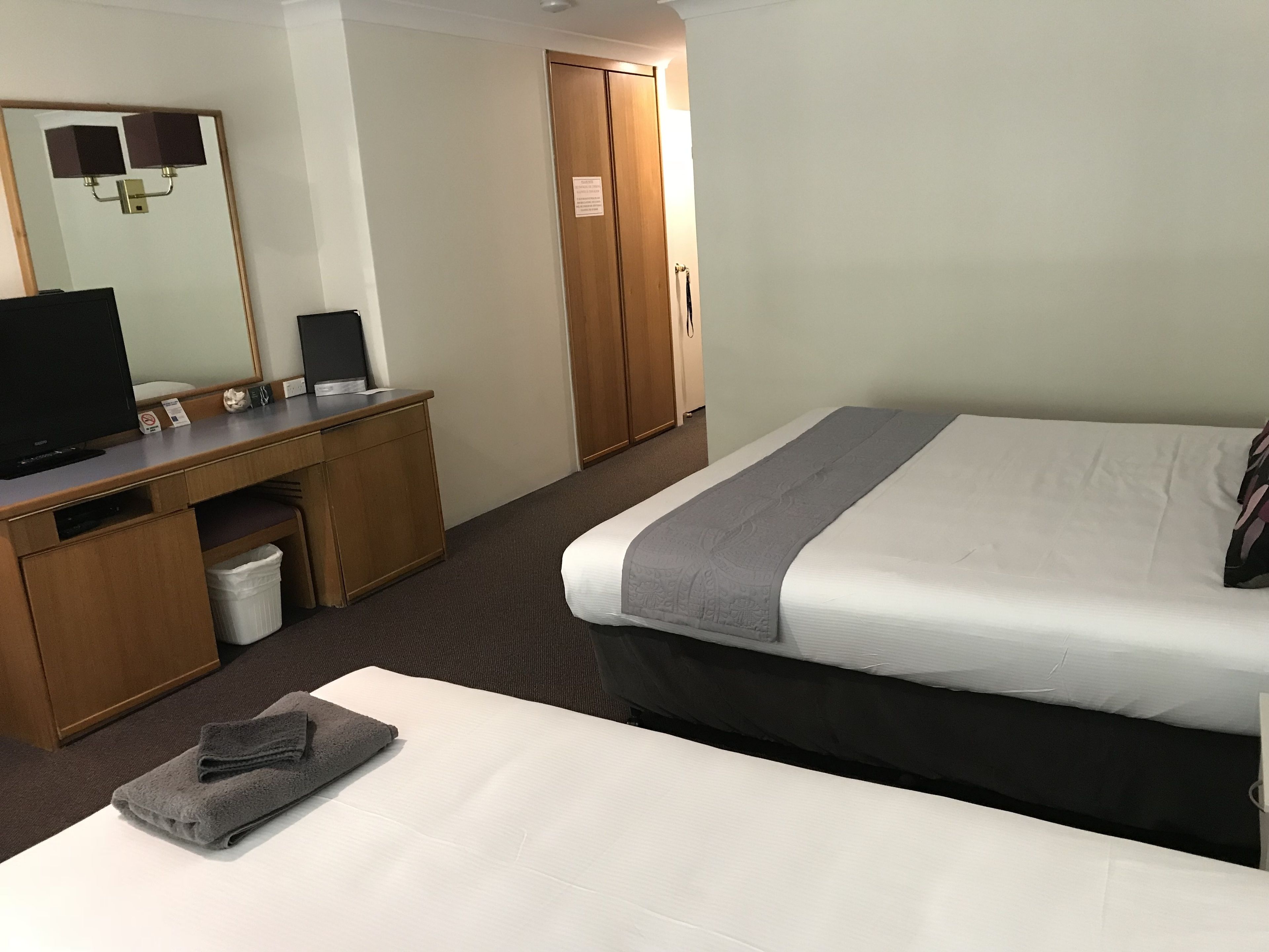 A hotel room with a bed, a desk with a computer, a television, and a mirror.