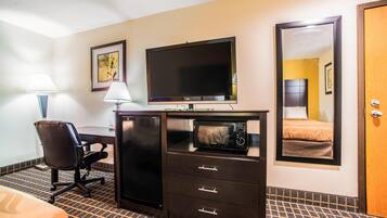 Una habitación de hotel con escritorio, silla, televisión, espejo y una cama.