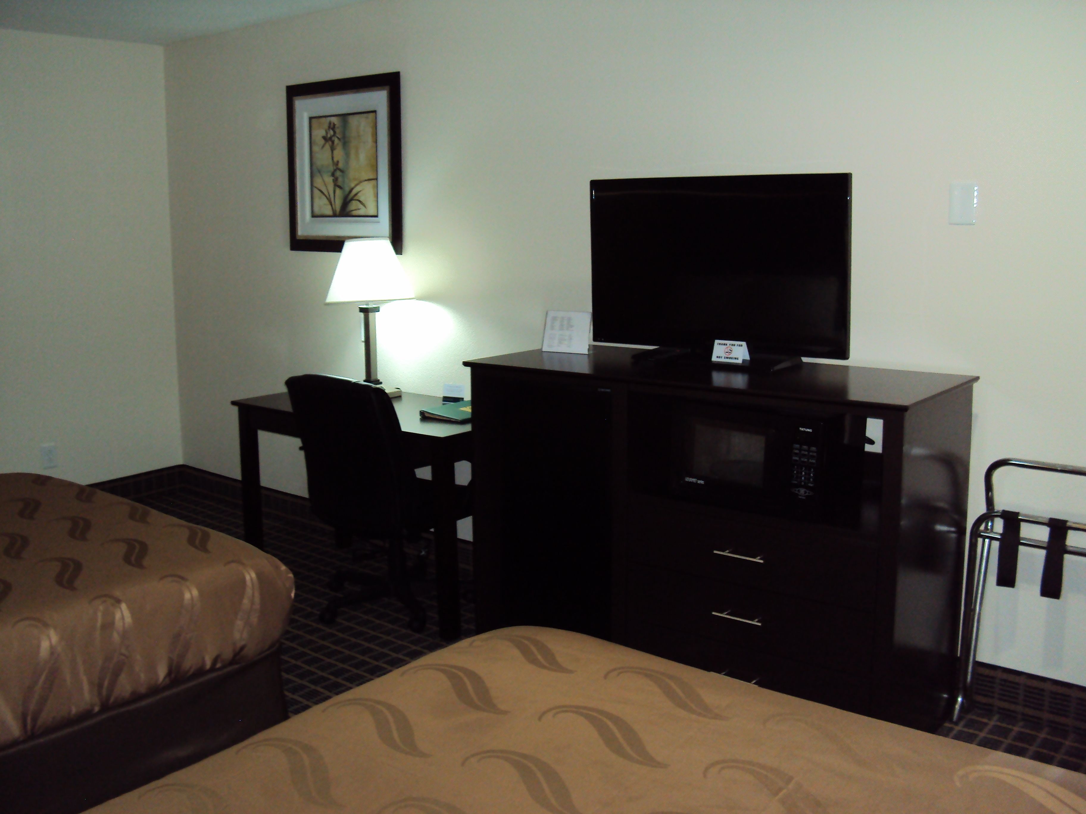 Habitación de hotel con una cama, un escritorio con televisor, una lámpara y una silla.