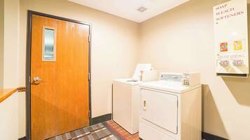 A laundry area with a wooden door, two washing machines, and a poster on the wall advertising soap and bleach softeners.