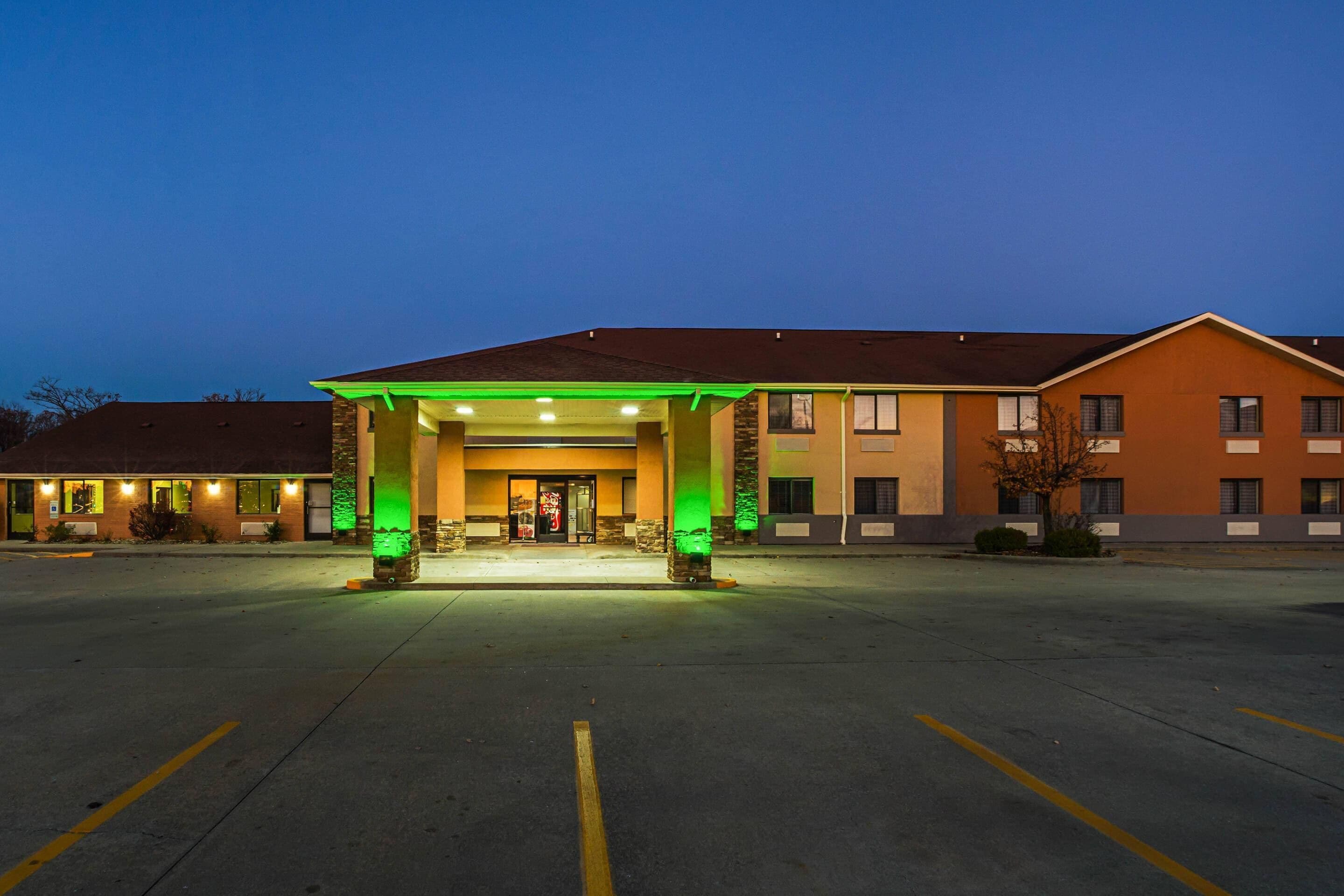 Entrada de hotel con zona cubierta, estacionamiento y un edificio de múltiples ventanales.