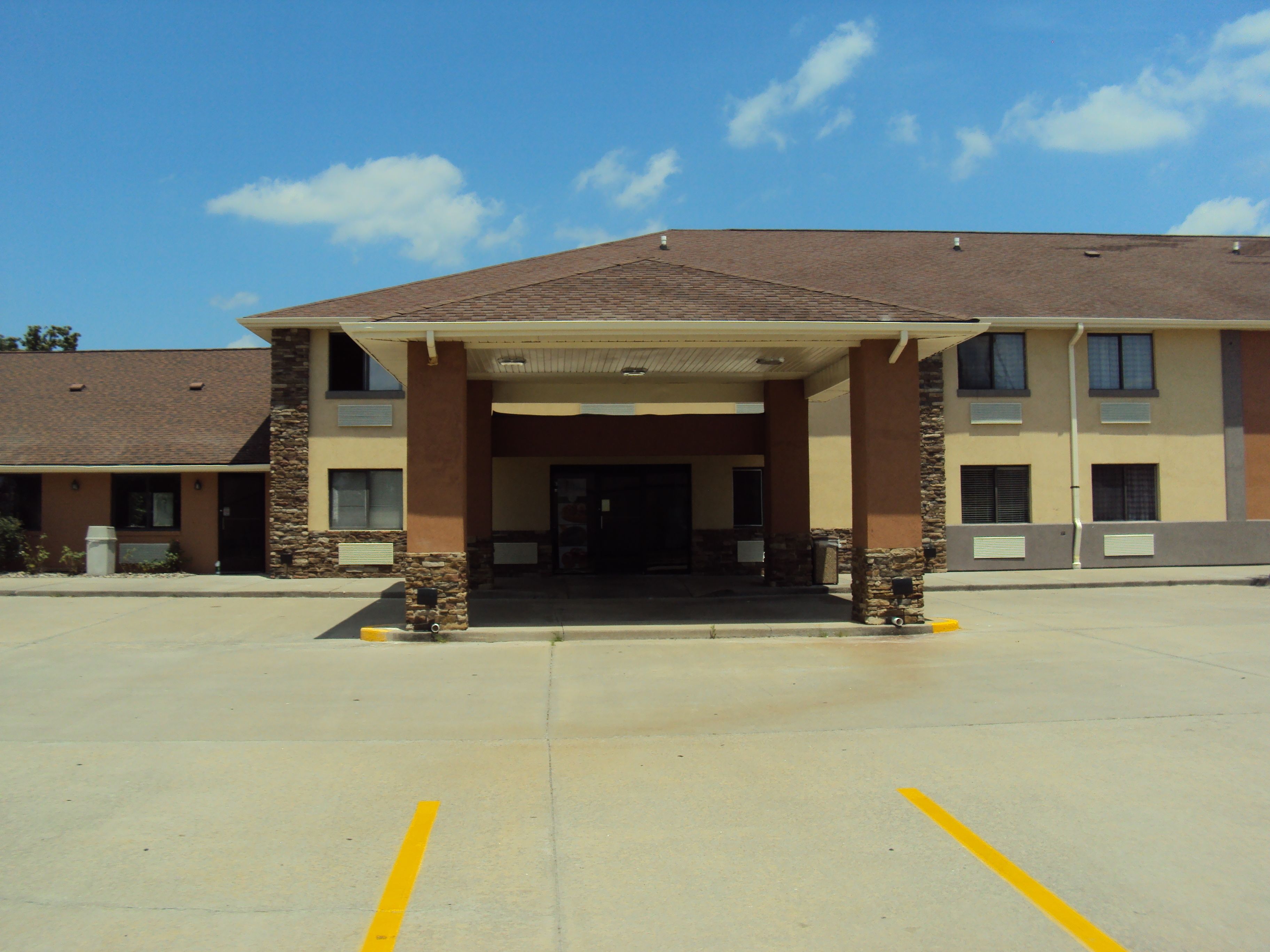 A hotel with a covered entrance, a parking lot, and a clear sky.