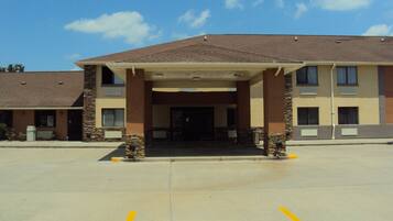 A hotel with a covered entrance, a parking lot, and a clear sky.