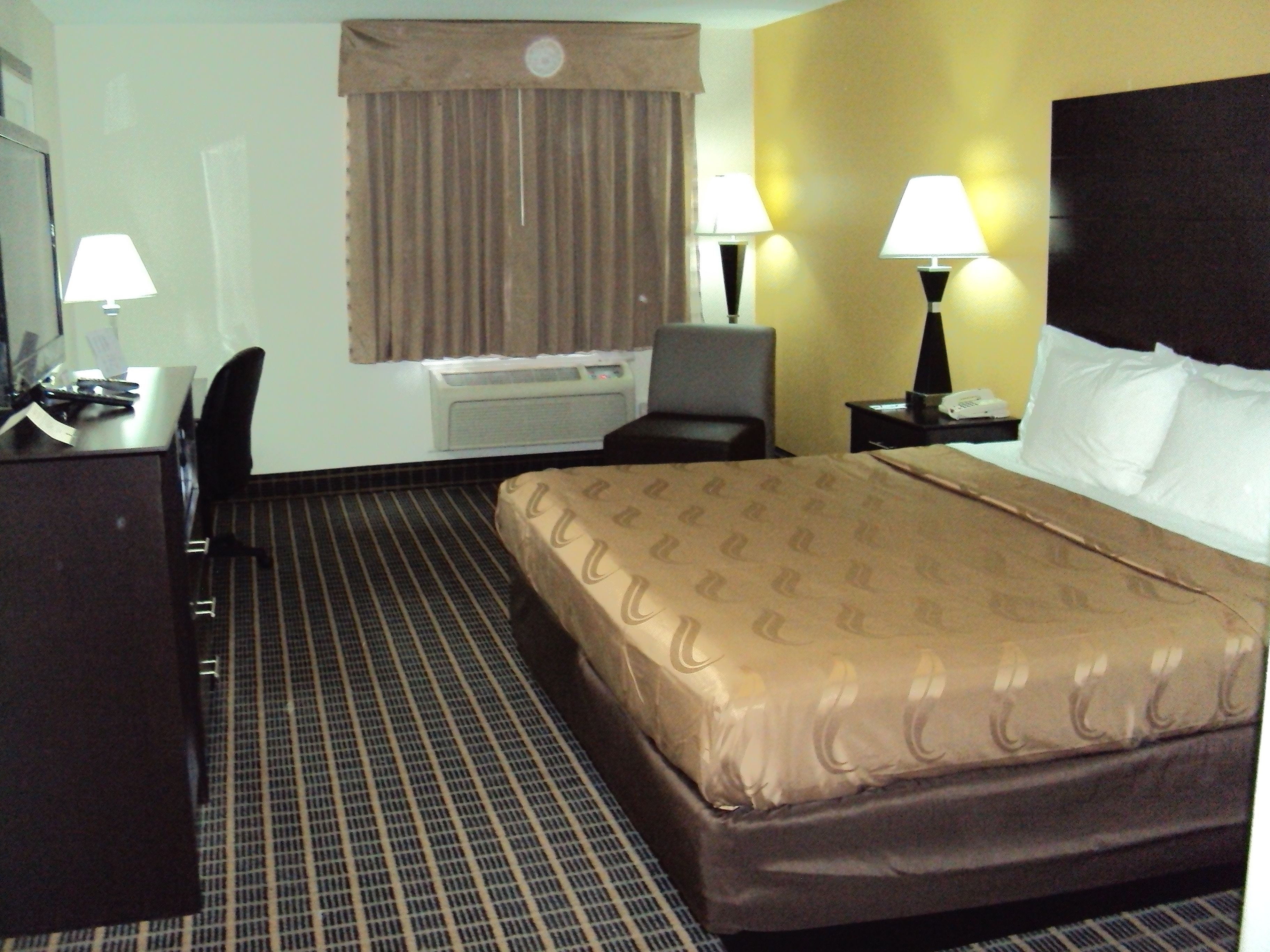 Habitación de hotel con cama, escritorio, silla, dos lámparas y teléfono.