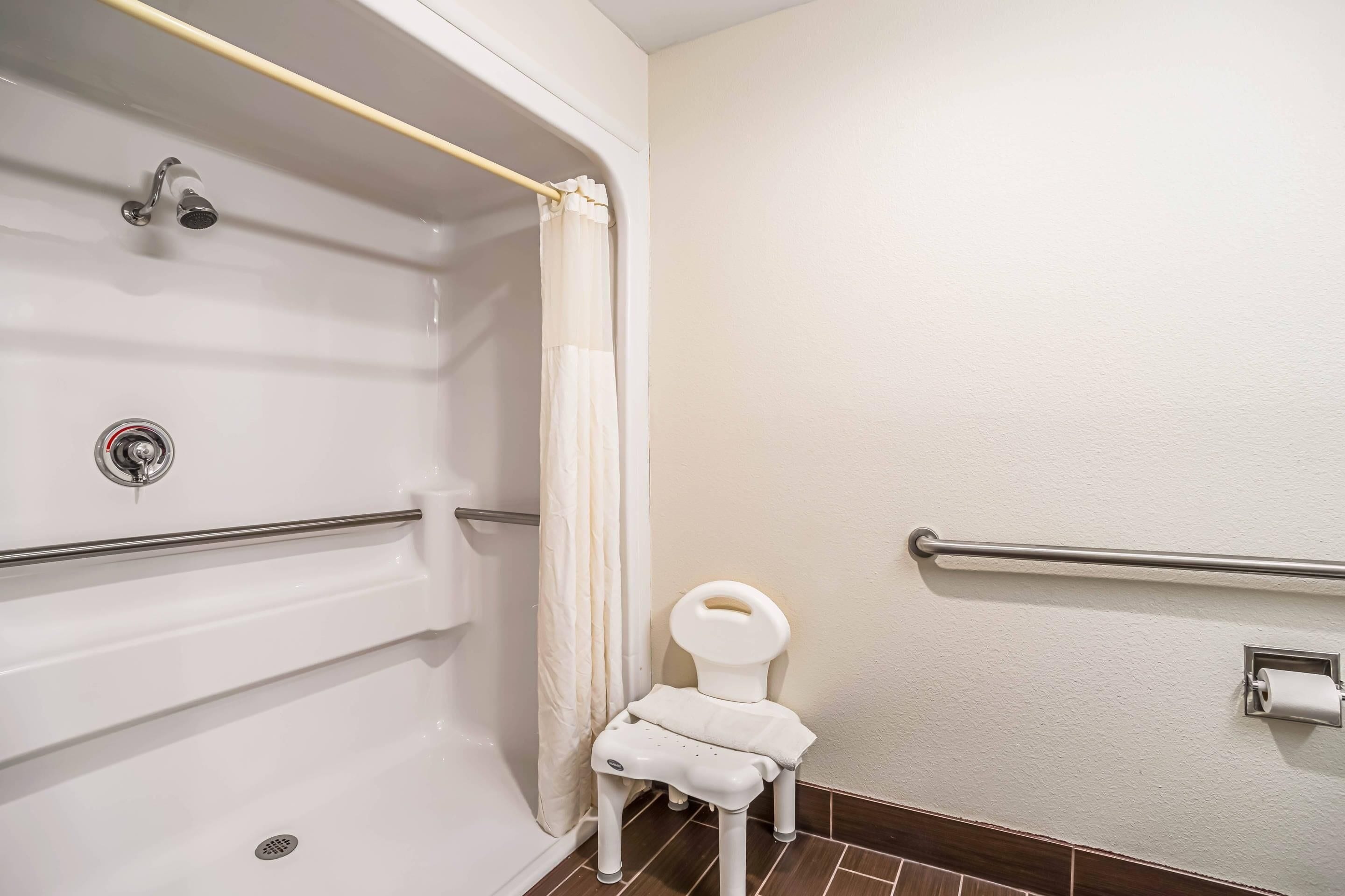 A bathroom with a shower, toilet, and grab bars.
