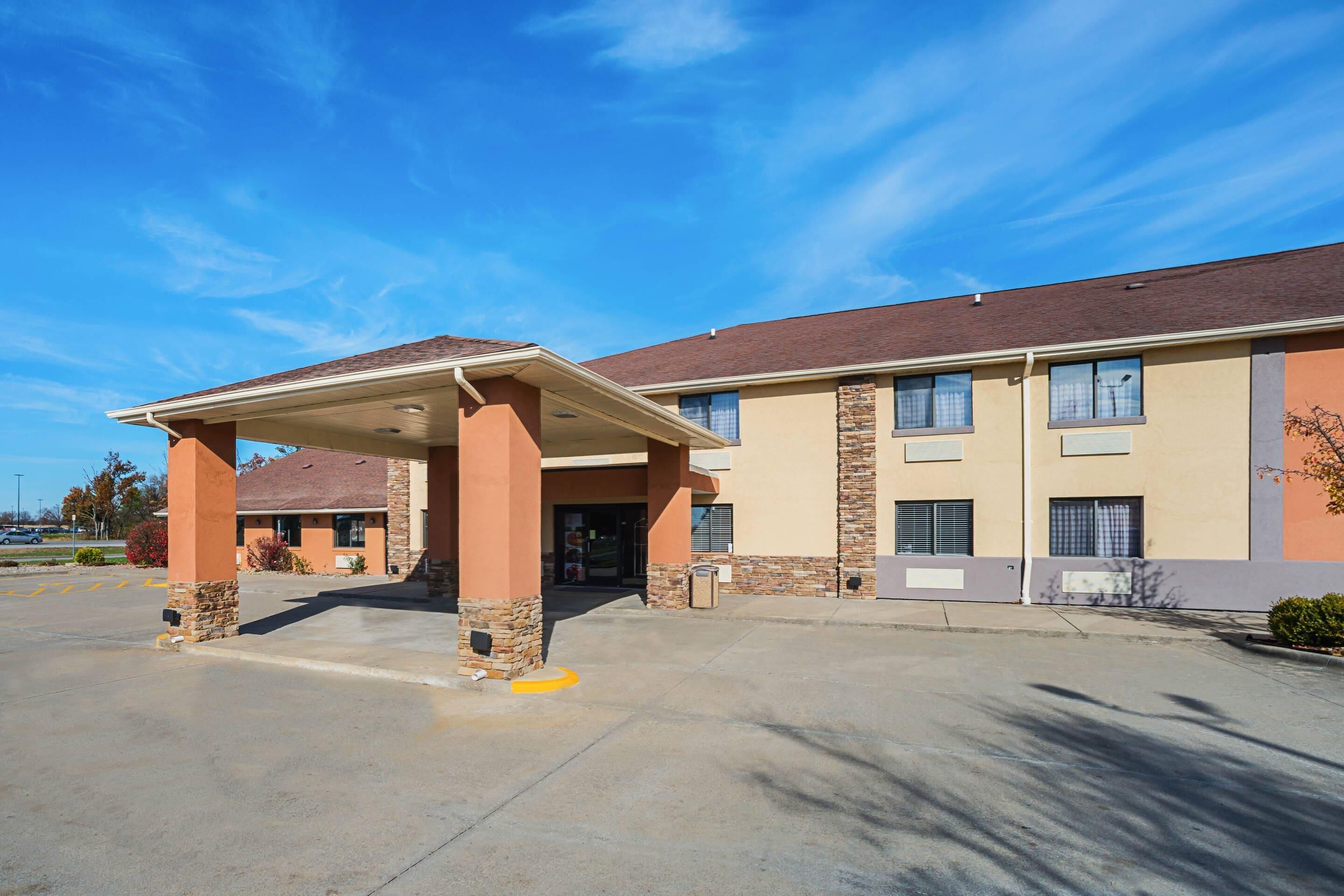 A hotel with a covered entrance, a parking lot, and a clear blue sky.