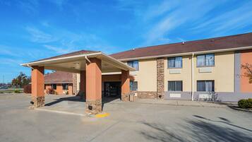 A hotel with a covered entrance, a parking lot, and a clear blue sky.