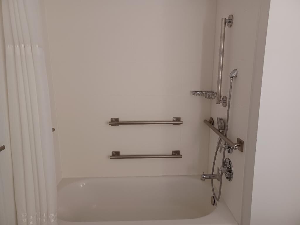A bathroom with a bathtub, two grab bars, a showerhead, and a faucet.