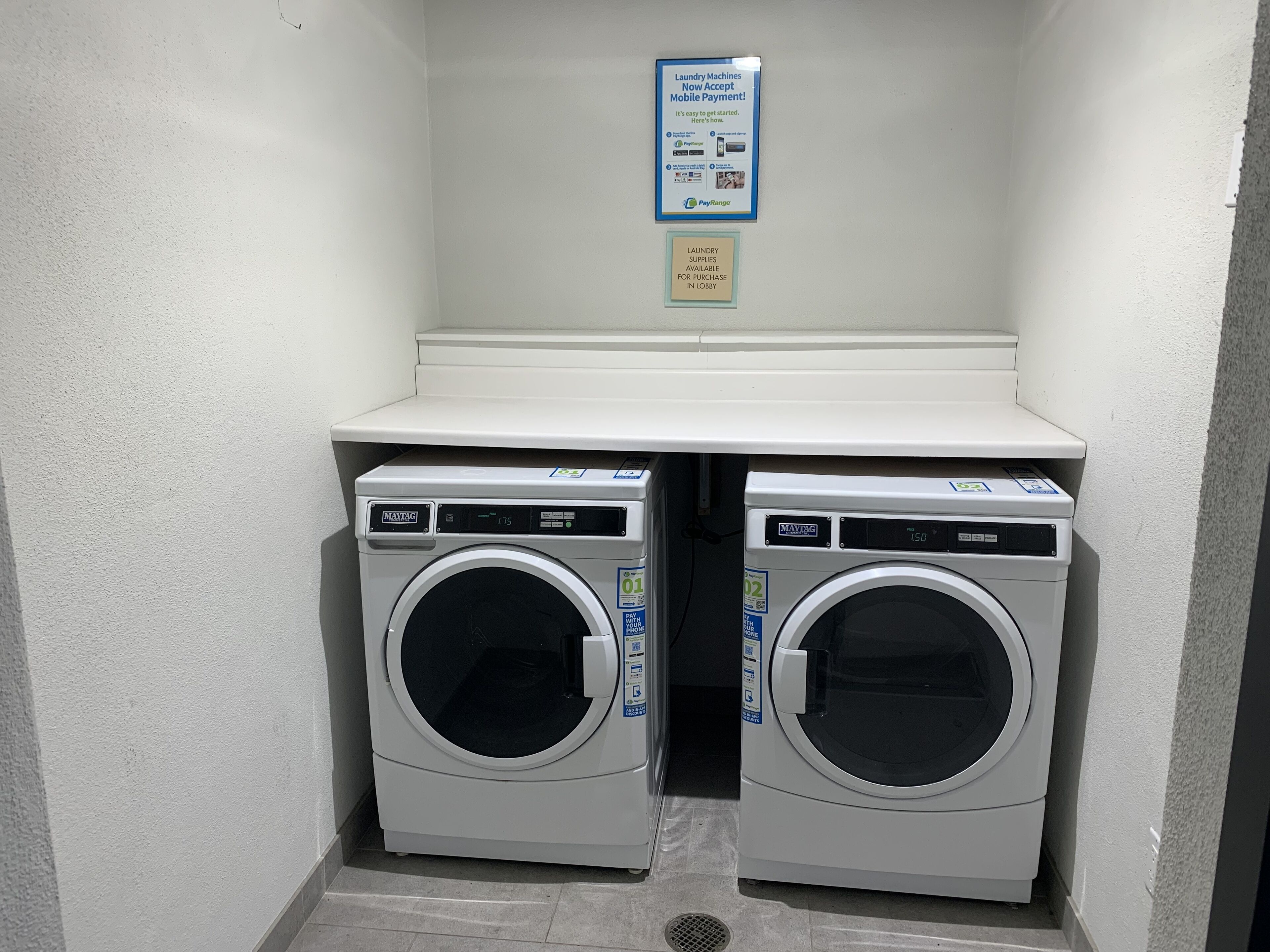 A laundry facility with two Maytag washing machines, a PayRange mobile payment sign, and a notice about laundry supplies.