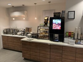 Una barra de desayuno con varios dispensadores de alimentos, una máquina de café y una pantalla digital que muestra granos de café.