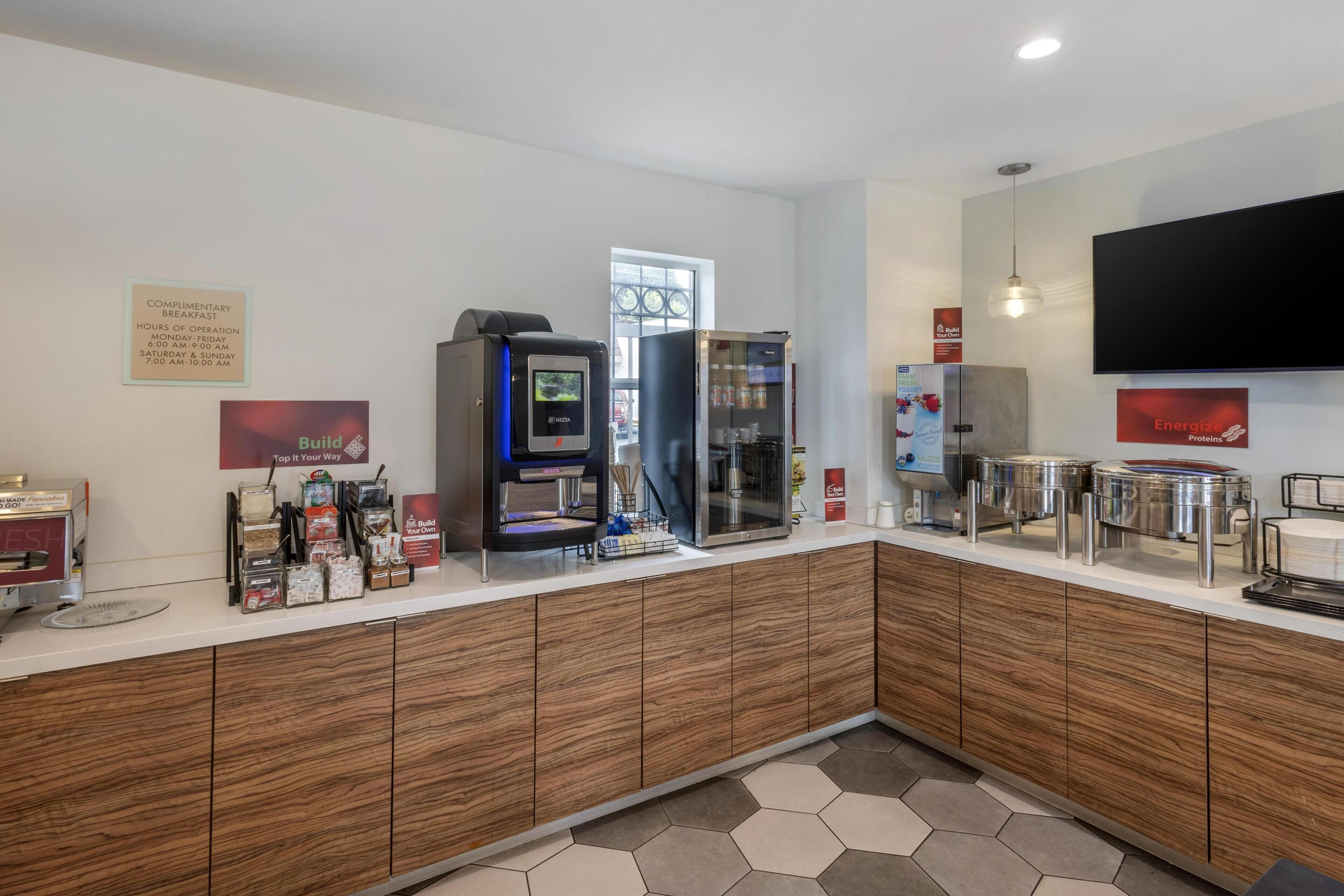 A modern kitchen area with a coffee machine, a refrigerator, and a flat-screen TV mounted on the wall.