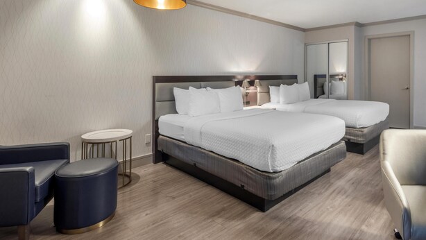 A hotel room with a large bed, a smaller bed, a round side table, a chair, and a lamp. - Best Western Plus Executive Suites (Redwood City)