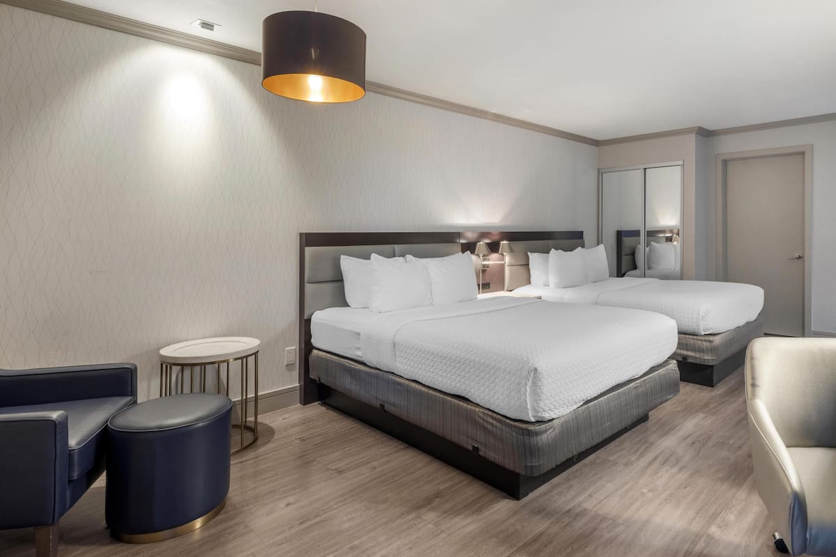 Una camera d'albergo con un letto grande, un letto più piccolo, un tavolino rotondo, una sedia e una lampada.