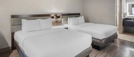 A hotel room with two beds, a wooden floor, and a nightstand with lamps.