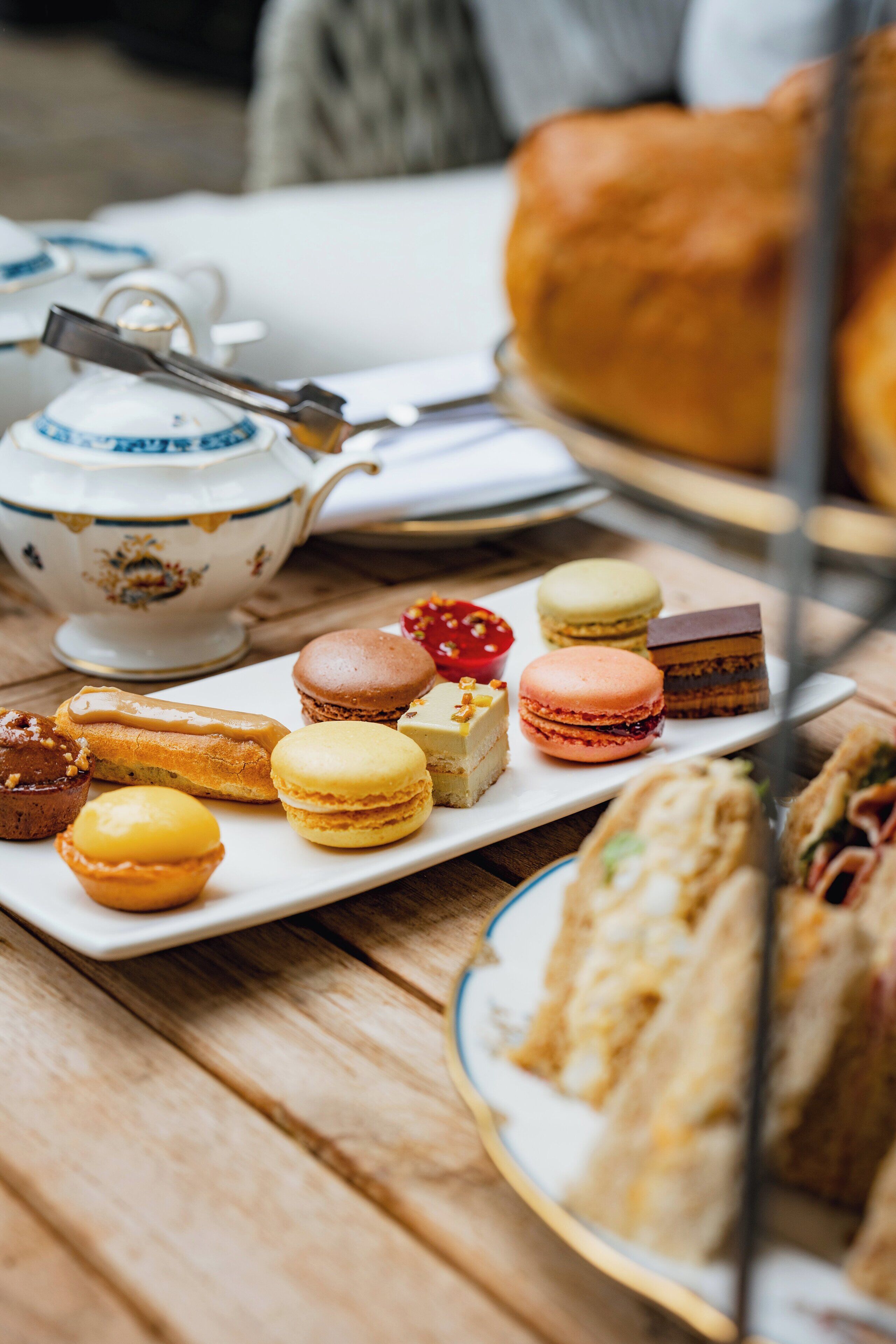 Uma mesa com diversos doces, sanduíches, um bule e uma xícara.