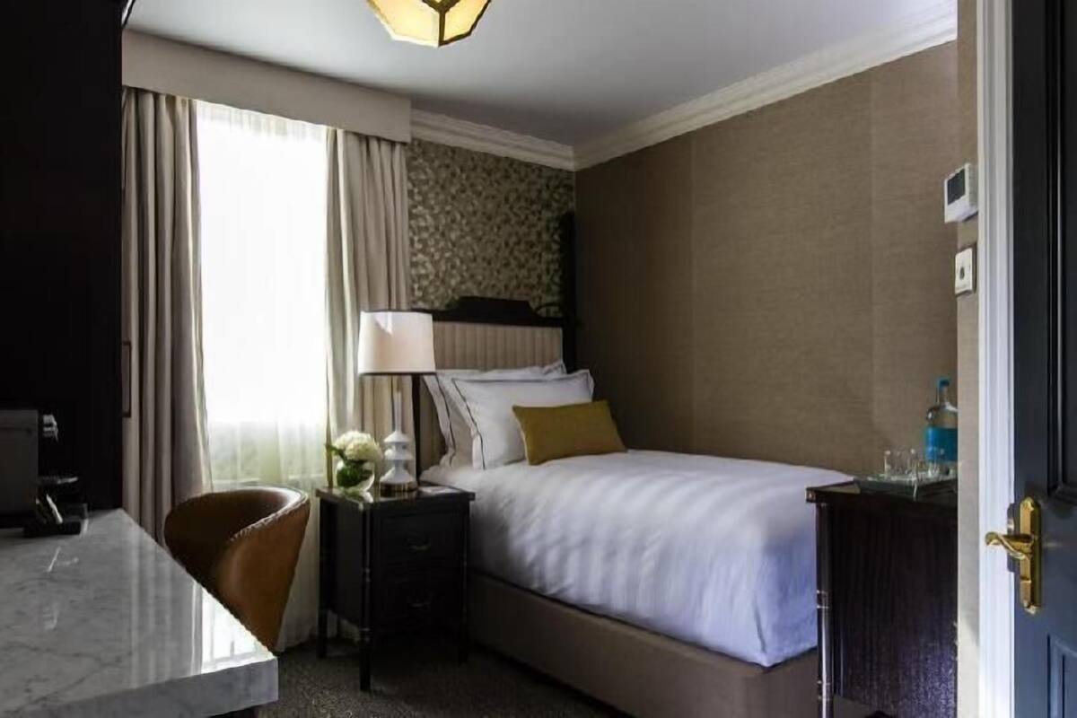 A hotel room with a bed, bedside table, lamp, chair, and a door.