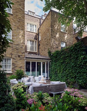 A brick house with a covered patio area featuring outdoor furniture and a variety of plants. - The Academy - Small Luxury Hotels of the World (London)