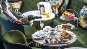 A table set with a tea set, sandwiches, pastries, and a bottle of champagne being poured. - The Academy - Small Luxury Hotels of the World (London)