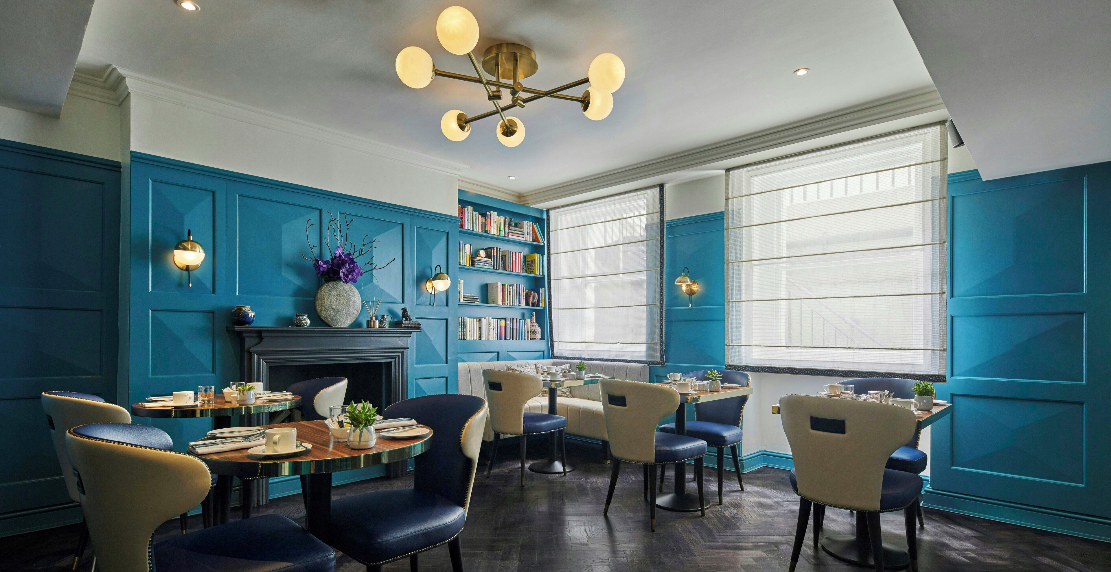 A dining area with blue paneled walls, a fireplace, bookshelves, and a chandelier.