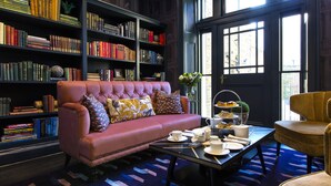 A cozy reading area with a leather sofa, a coffee table with tea cups, and a bookshelf filled with books. - The Academy - Small Luxury Hotels of the World (London)