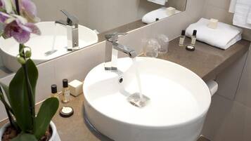 A bathroom with a white sink, two faucets, a mirror, and toiletries on the counter.