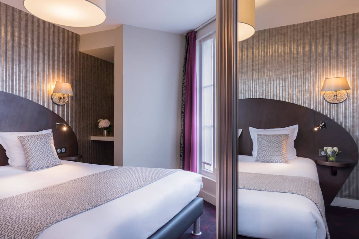 A hotel room with two beds, a large mirror, wall sconces, and a window with curtains.