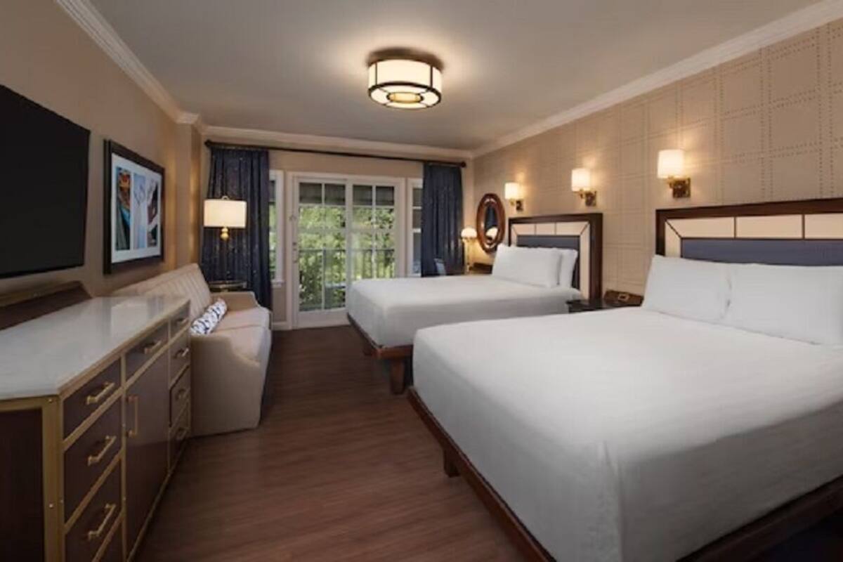 A hotel room with two beds, a desk, a dresser, and a view of the outdoors.