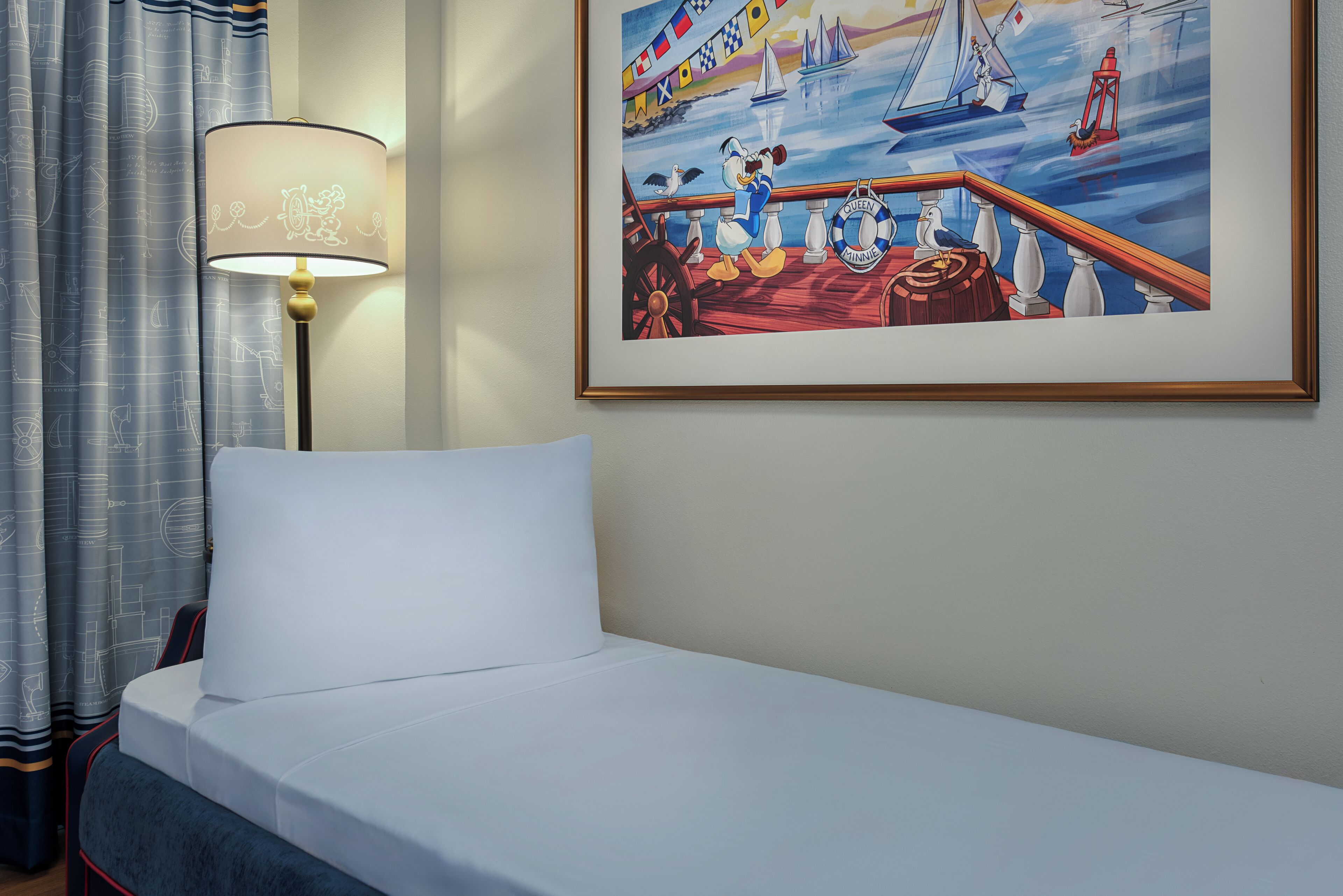 Ein Hotelzimmer mit einem Bett, einer Lampe und einem gerahmten Gemälde, das ein Meerbild zeigt.