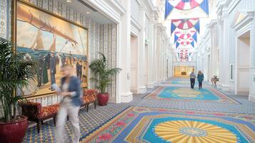 A grand hotel lobby with a large nautical-themed mural, ornate columns, and a patterned carpet.